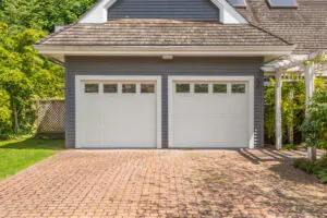 Two white garage doors, brick driveway.
