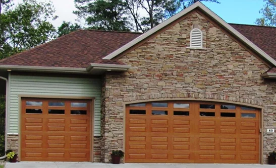 Wood-look brown fiberglass garage doors on a stone-facade home.