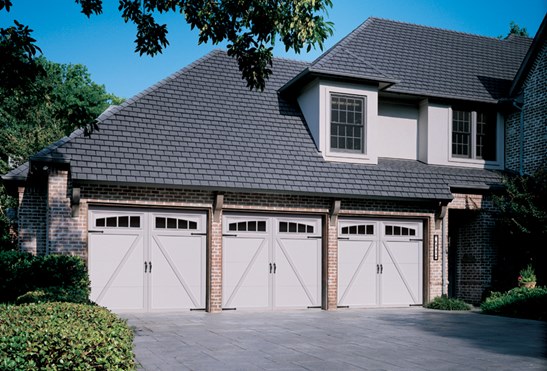 Carriage-style garage doors on three-car garage of a large home with gray and brick exterior.