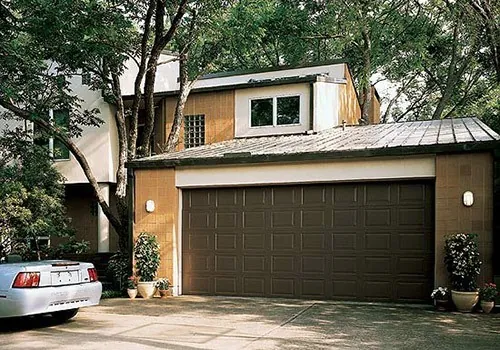 Brown garage door on a yellow/tan home surrounded by trees.