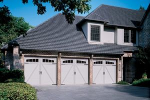 Three-car garage door installation with white garage doors with small windows in the top.
