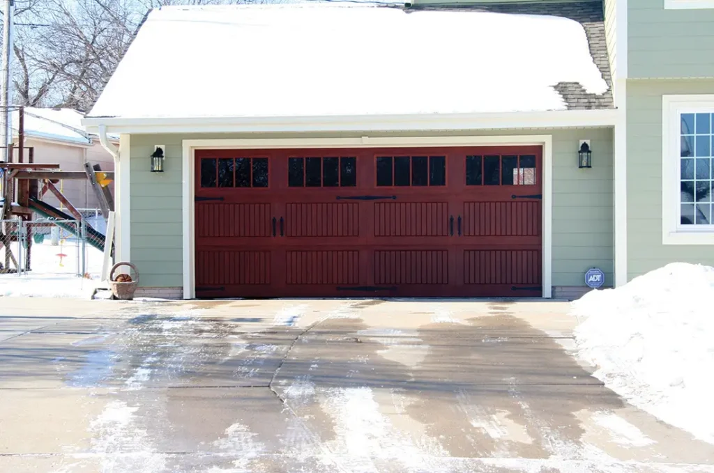 Residential dark red garage door with snow on the roof and driveway